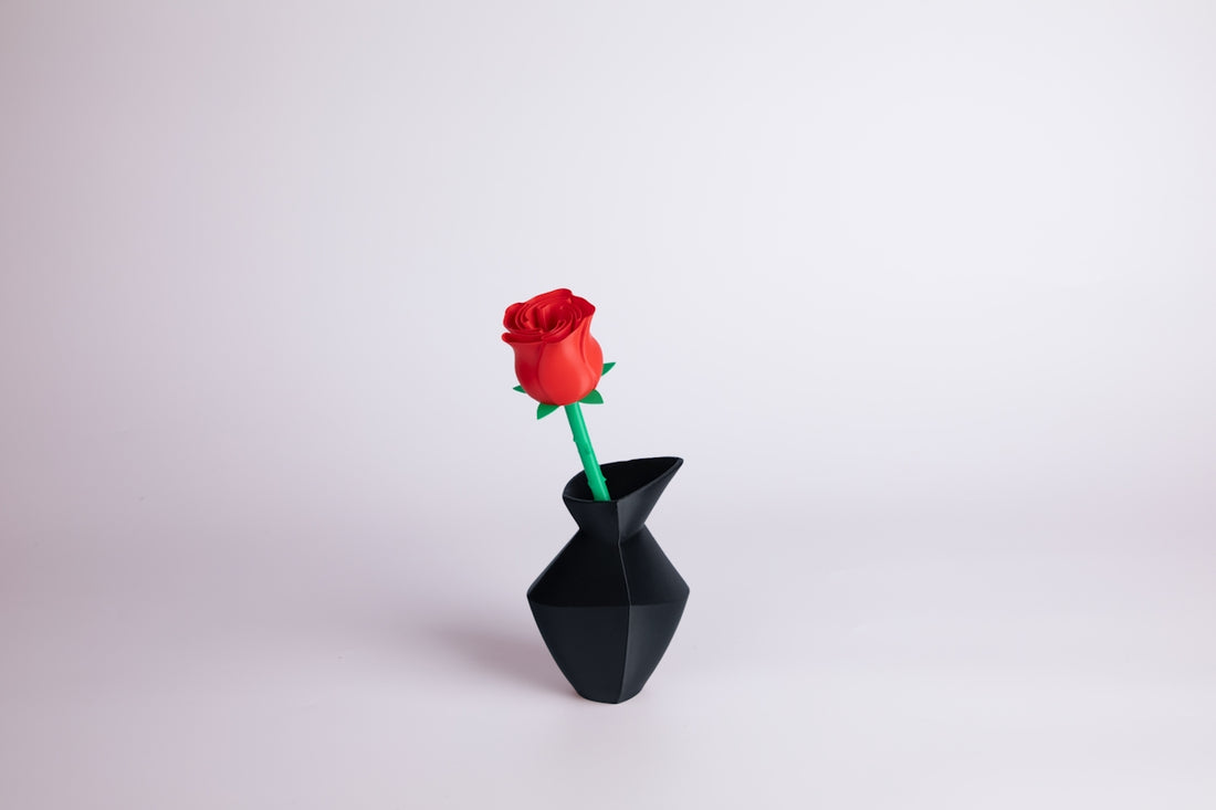 A red rose sits in a black origami vase.